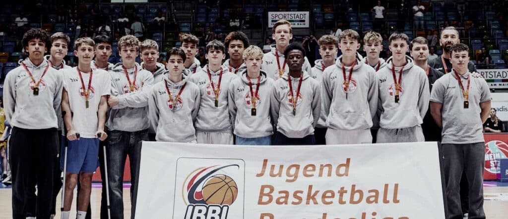 Jugendbasketballmannschaft der RheinStars Köln mit Medaillen und Banner bei Siegerehrung.