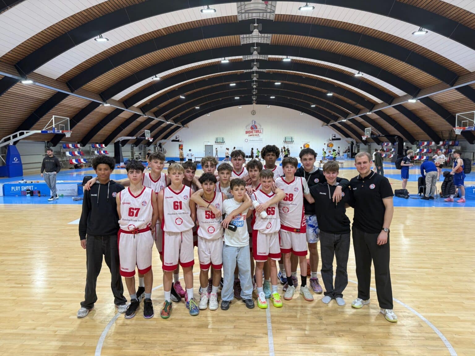 Basketballmannschaft der RheinStars Köln posiert mit Trainern in einer Sporthalle.