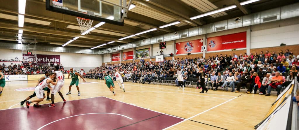 Basketballspiel der RheinStars Köln in vollbesetzter Sporthalle mit Zuschauern.