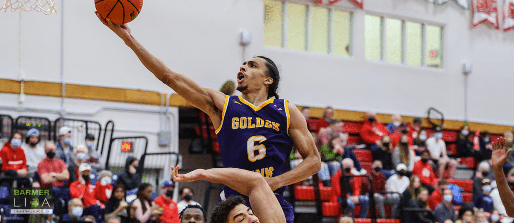 Basketballspieler der Goldes springt mit Ball zum Korb, Zuschauer im Hintergrund.