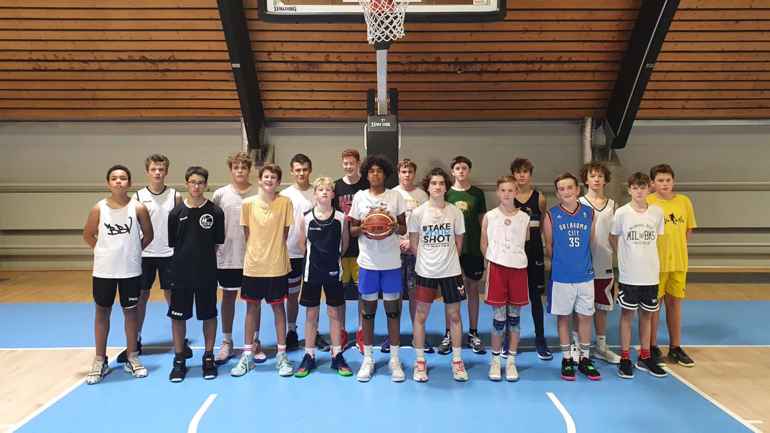 Etwa 18 Jugendliche der RheinStars Köln stehen in einer Sporthalle unter einem Basketballkorb.