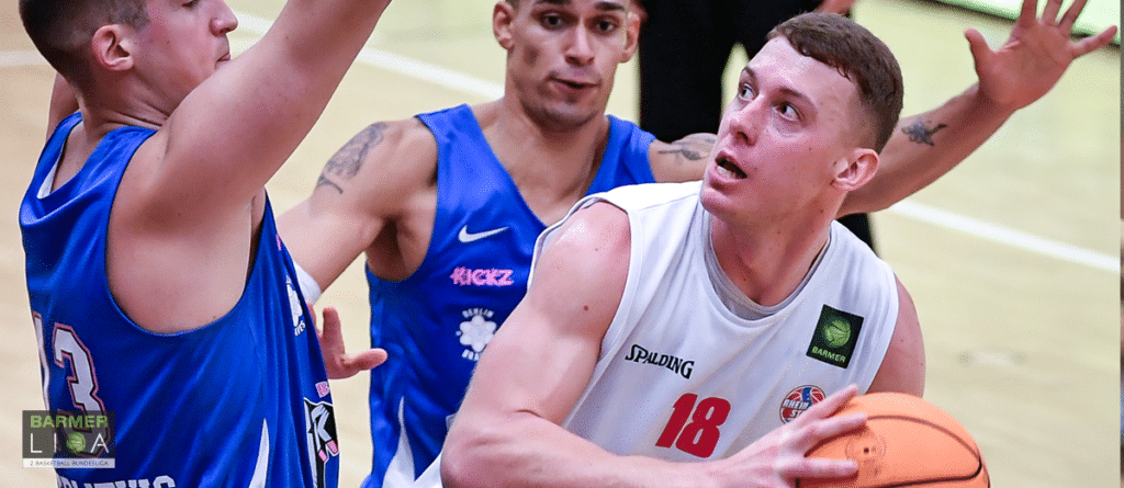 Basketballspiel: Spieler der RheinStars Köln in weißem Trikot mit Nummer 18 dribbelt gegen blaue Gegner.