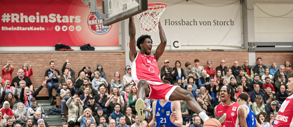Basketballspieler der RheinStars Köln dunkt Ball in voller Halle vor Publikum.