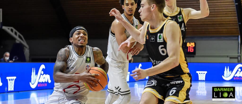 Basketballspiel: RheinStars-Spieler mit Ball gegen Gegner in schwarzem Trikot.