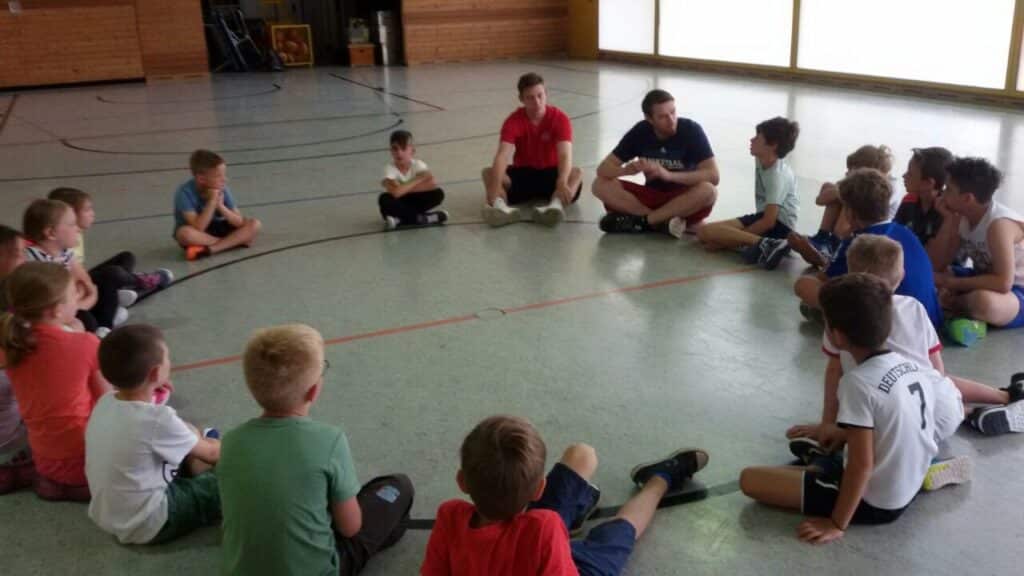 Kinder der RheinStars Köln sitzen im Kreis auf dem Hallenboden während einer Trainingseinheit.