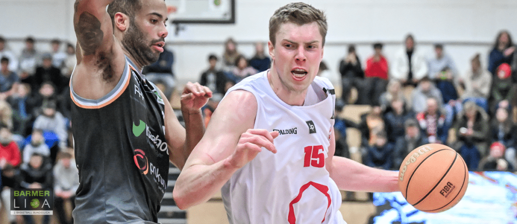 Basketballspiel der RheinStars Köln: Spieler Nummer 15 in weißem Trikot dribbelt gegen Gegner in schwarzem Trikot.