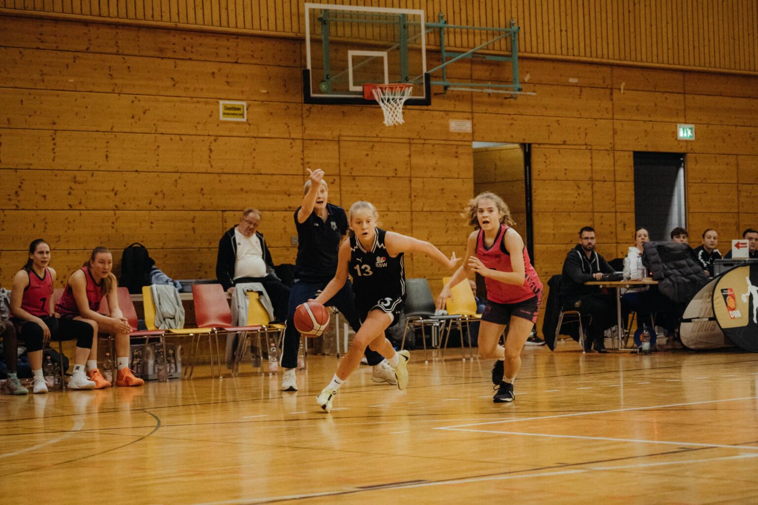 Basketballspiel der RheinStars Köln in einer Sporthalle mit Spielerinnen in schwarzen und roten Trikots.