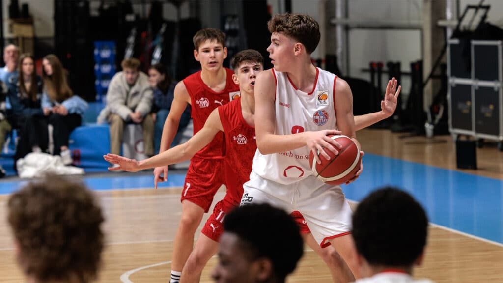 Basketballspiel der RheinStars Köln: Spieler in Weiß mit Ball gegen Gegner in Rot.