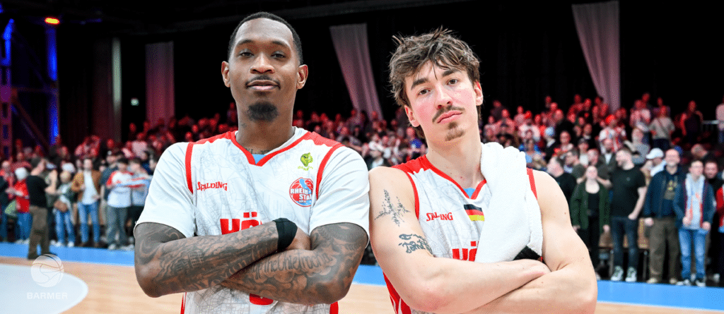 Zwei Basketball-Spieler der RheinStars Köln stehen mit verschränkten Armen vor Zuschauern.
