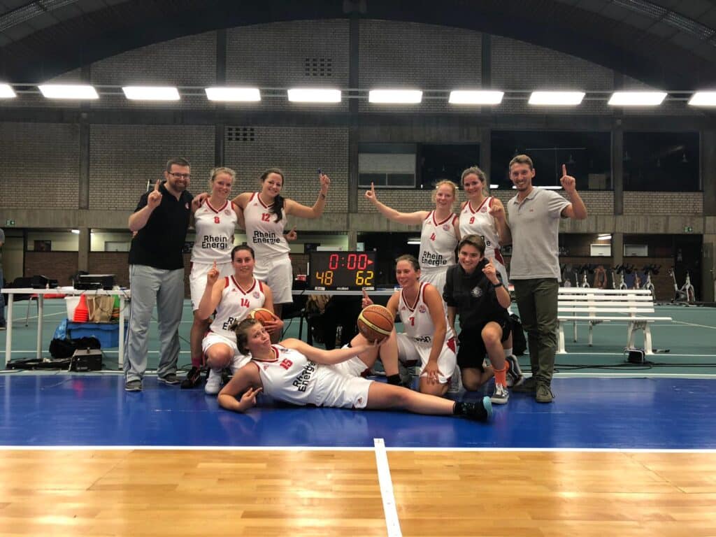 Basketballteam RheinStars Köln jubelt nach Sieg in Sporthalle.