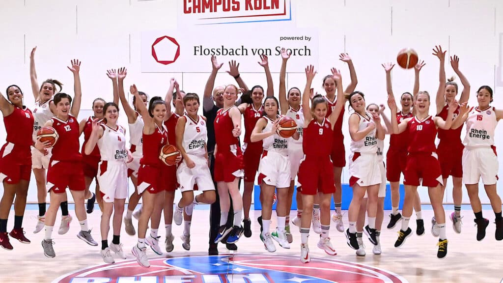 Die Basketballmannschaft RheinStars Köln springt jubelnd auf dem Spielfeld, alle Arme erhoben.