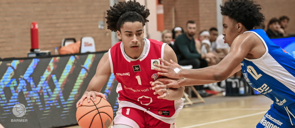 Basketballspieler der RheinStars Köln in rotem Trikot dribbelt gegen Verteidiger in blauem Trikot.