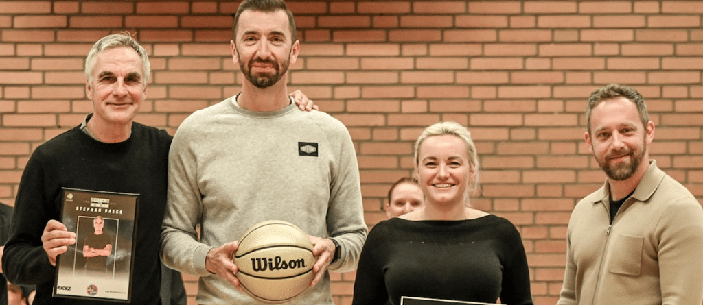 Vier Personen der RheinStars Köln posieren vor Backsteinwand mit Basketball und Urkunde.