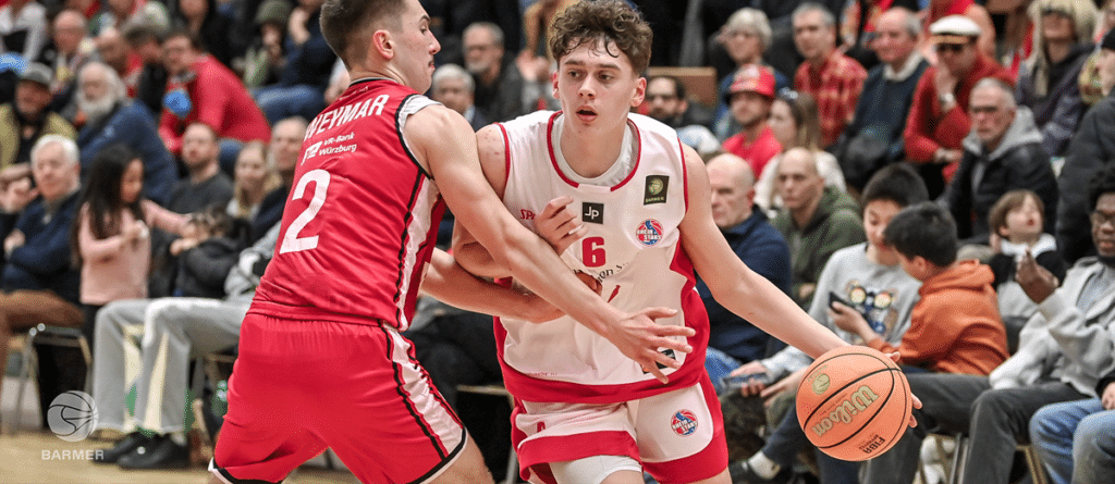 Basketballspieler der RheinStars Köln in rot-weißem Trikot dribbelt gegen Gegner in rotem Trikot.