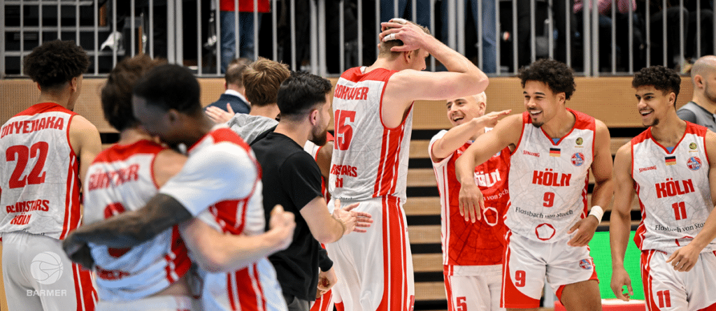 Basketballmannschaft RheinStars Köln feiert gemeinsam auf der Tribüne.