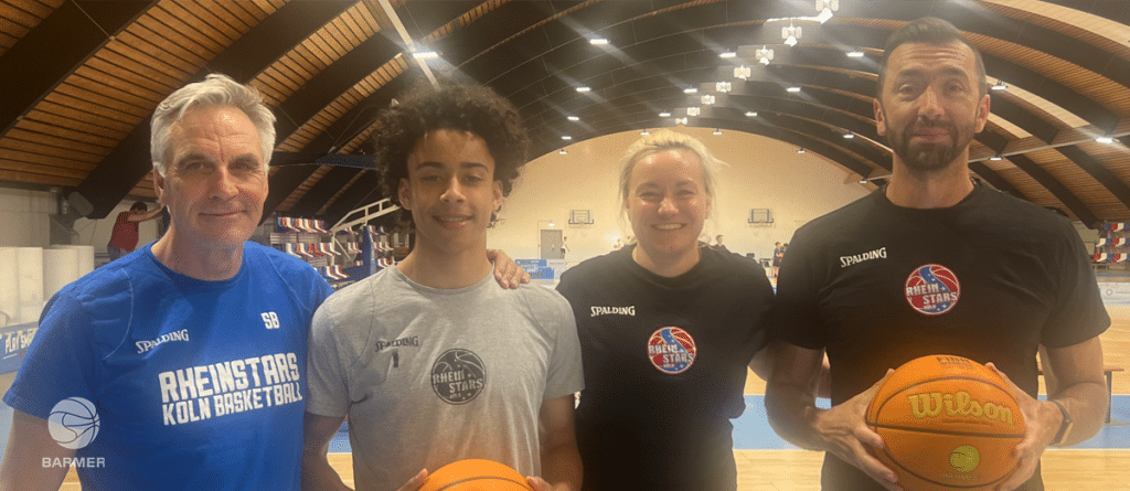 Vier Personen der RheinStars Köln Basketball posieren mit Basketbällen in der Sporthalle.