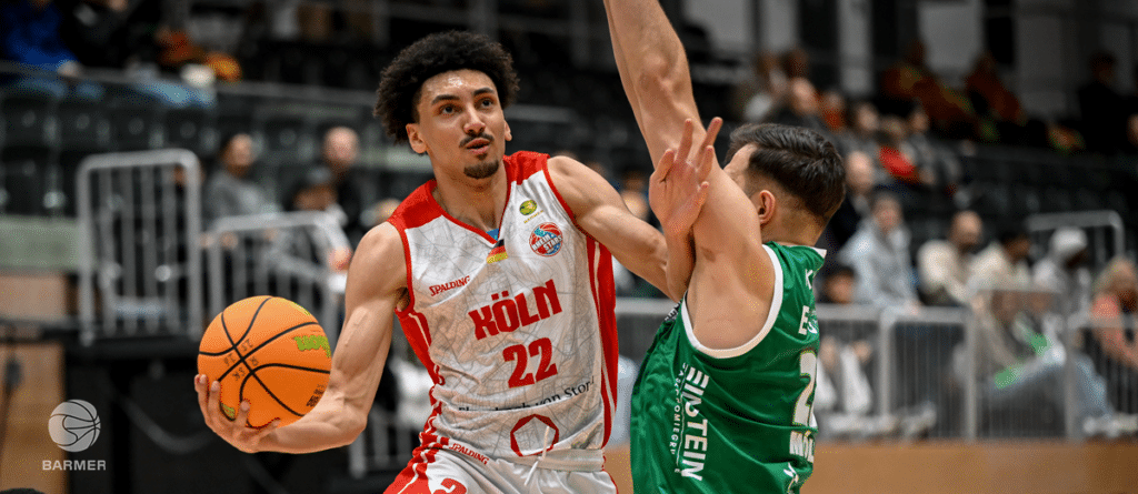 Basketballspieler der RheinStars Köln mit Nummer 22 dribbelt gegen grünen Gegenspieler.