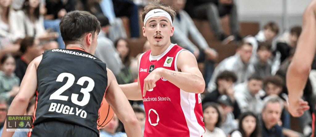 Basketballspieler der RheinStars Köln in rotem Trikot während eines Spiels gegen Gegner in schwarzem Trikot.