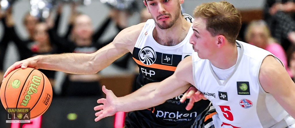 Basketballspiel der RheinStars Köln: Spieler in weißem Trikot mit Nummer 5 verteidigt gegen Gegner in schwarzem Trikot.