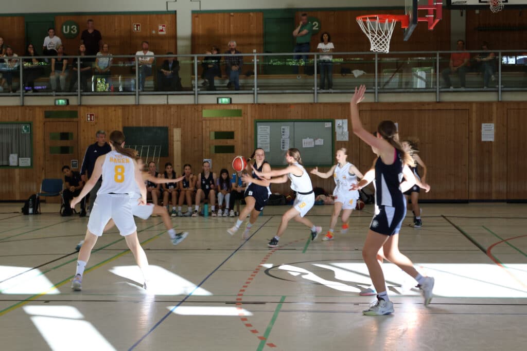 Basketballspiel der RheinStars Köln in einer Sporthalle mit Spielerinnen in weißen und dunkelblauen Trikots.