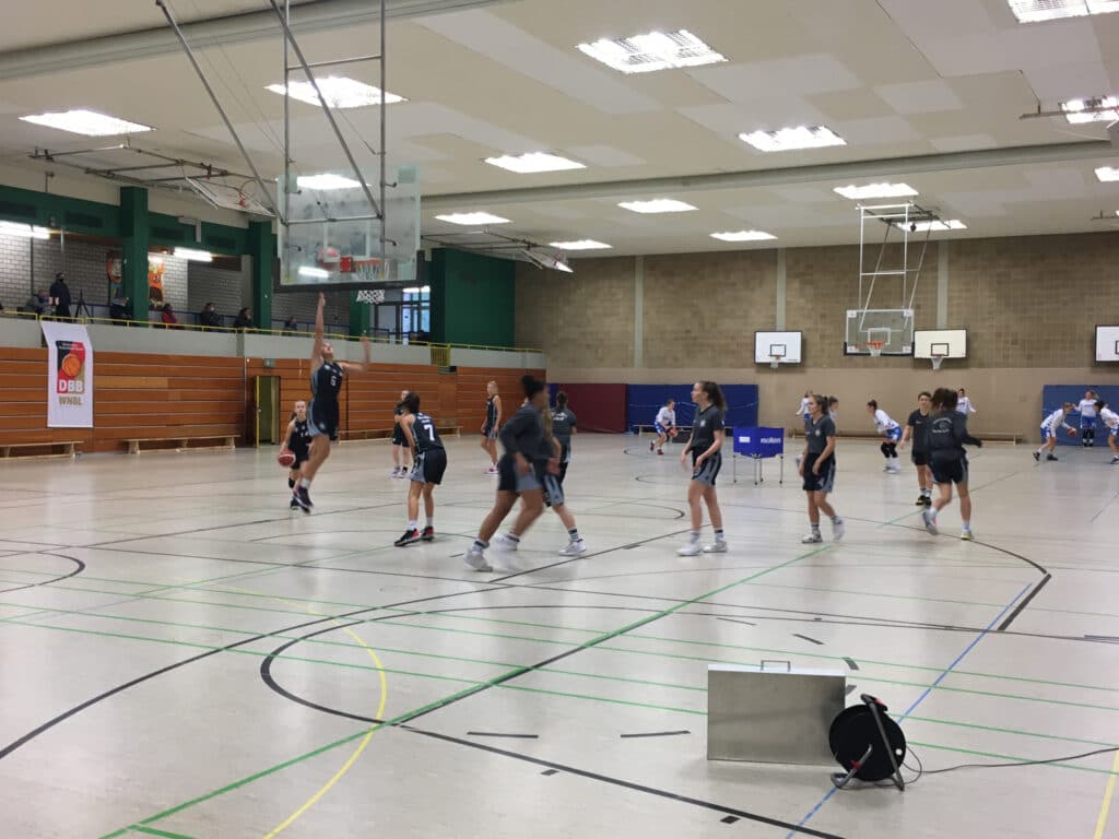Basketballtraining der RheinStars Köln in einer Sporthalle mit mehreren Körben und Spielerinnen in dunklen Trikots.
