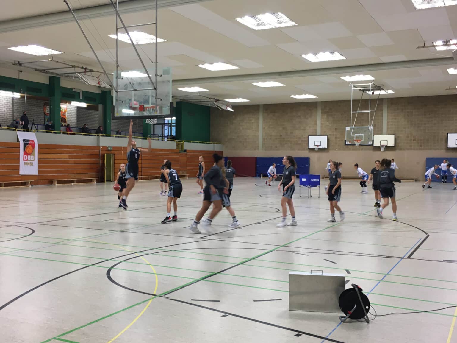Basketballtraining der RheinStars Köln in einer Sporthalle mit mehreren Körben und Spielerinnen in dunklen Trikots.