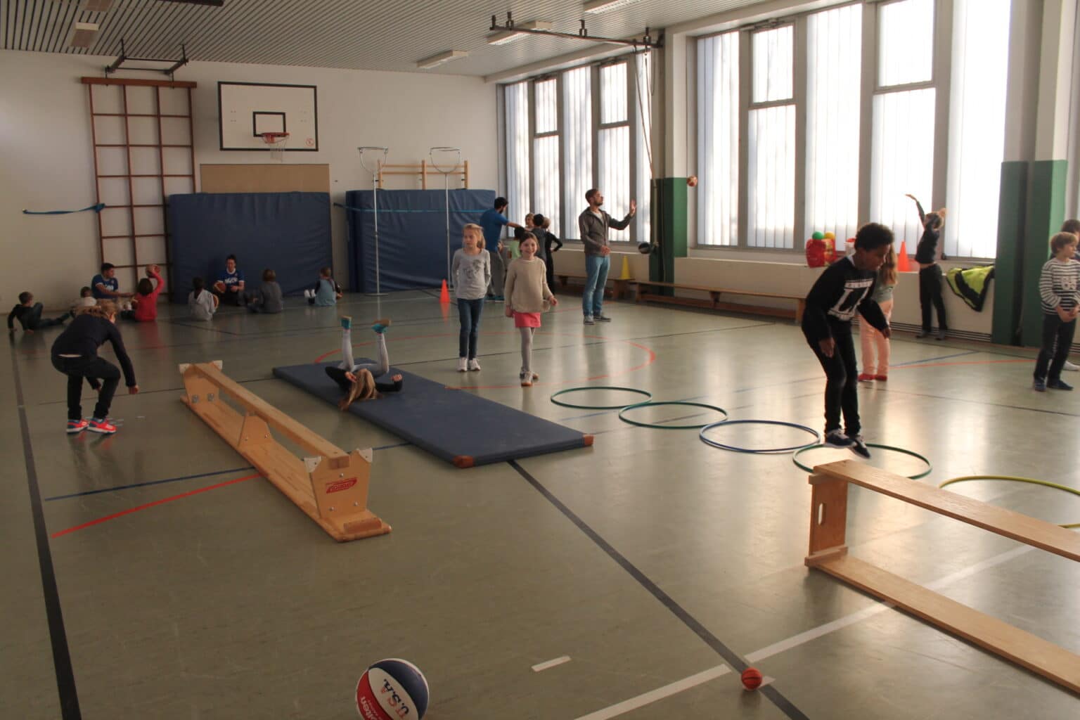 Sporthalle mit Kindern bei Bewegungsübungen der RheinStars Köln; Geräte wie Balken, Matten und Ringe sind aufgebaut.