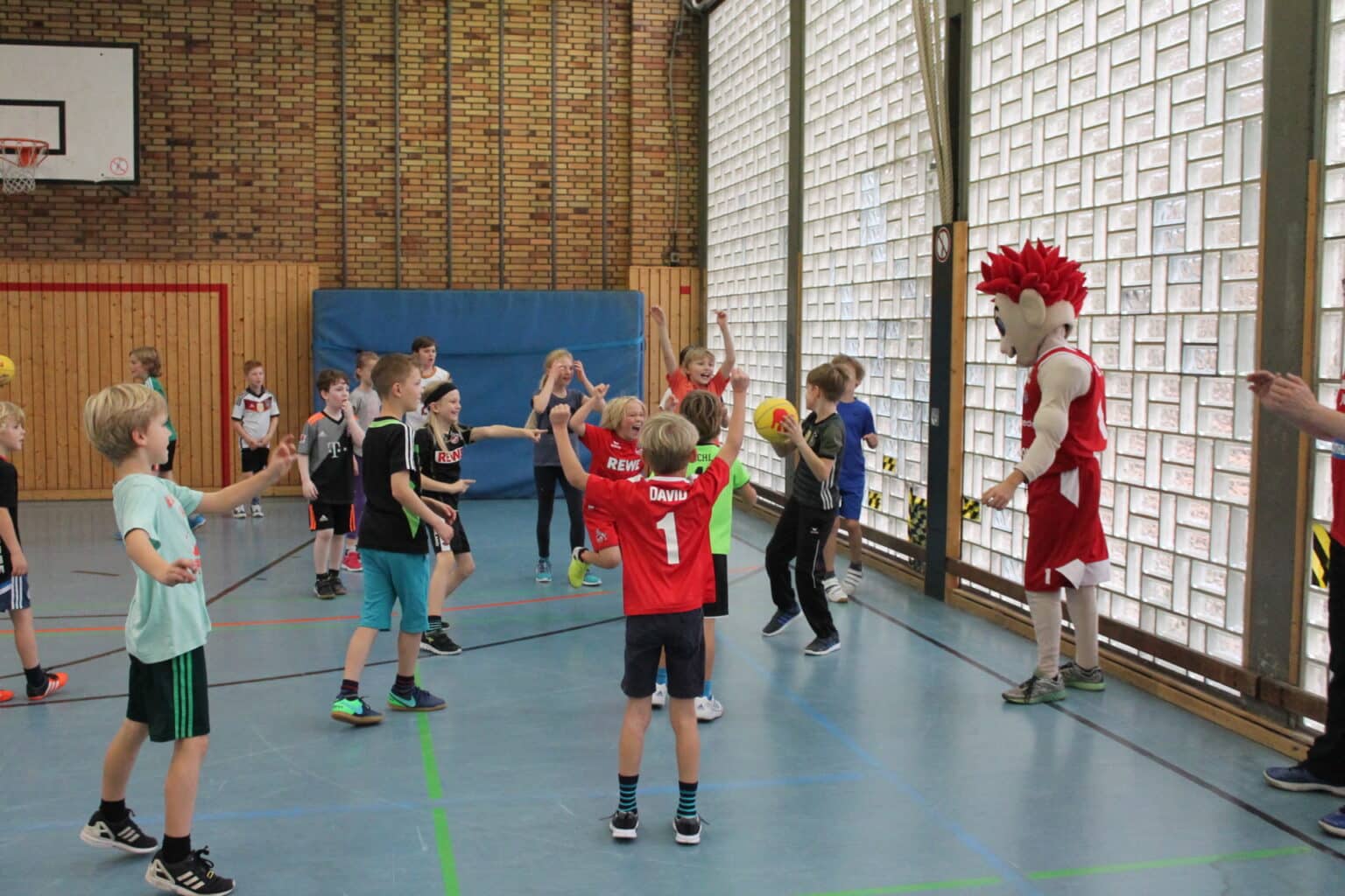 Kinder trainieren in einer Sporthalle der RheinStars Köln mit einem Maskottchen.