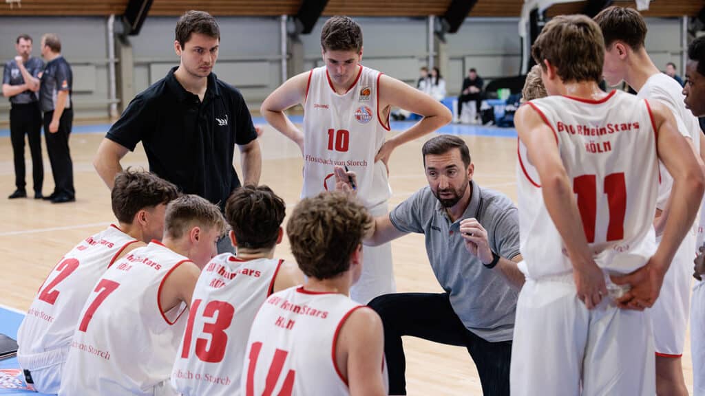 Trainer der RheinStars Köln gibt Anweisungen an seine Basketballmannschaft während einer Spielzeitpause in der Sporthalle.