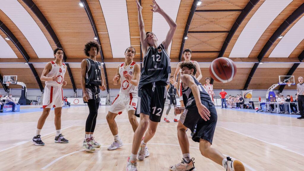 Basketballspiel der RheinStars Köln: Spieler in weißen und schwarzen Trikots kämpfen um den Ball in einer modernen Sporthalle.