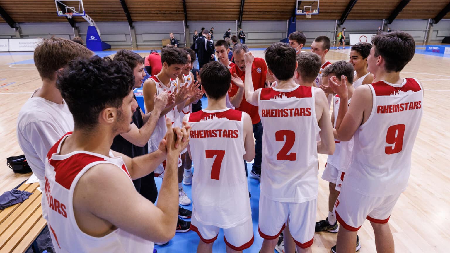 Basketballmannschaft RheinStars Köln steht im Kreis zusammen und motiviert sich gegenseitig in der Halle.