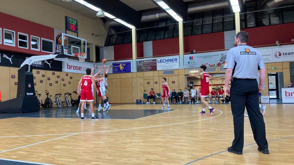 Basketballspiel der RheinStars Köln in einer Sporthalle mit roten und weißen Teams sowie Schiedsrichter.