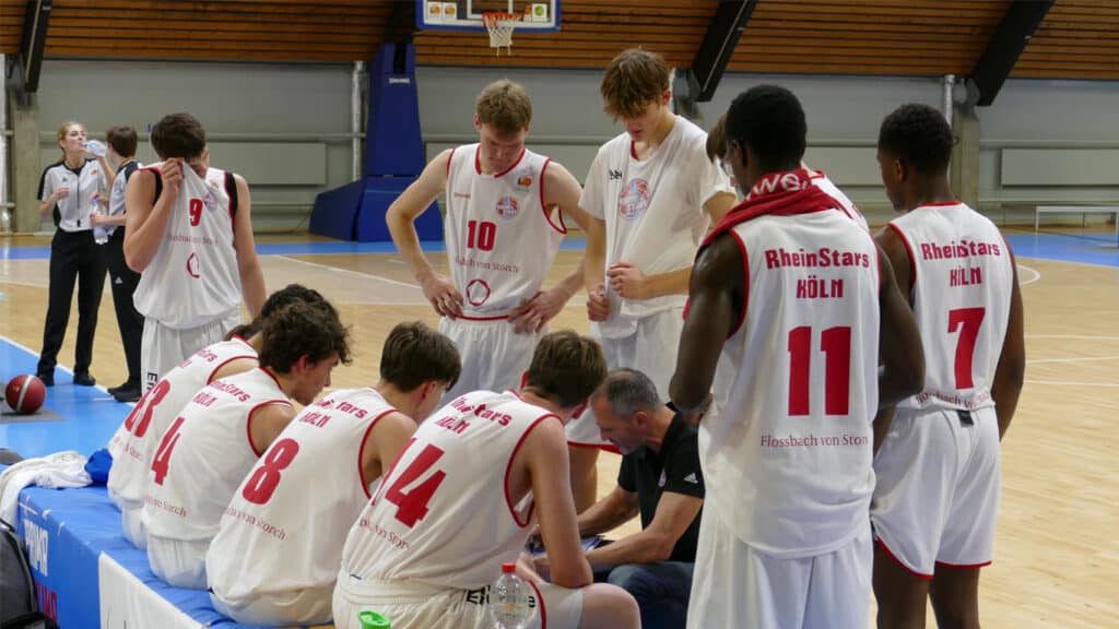 RheinStars Köln-Basketballteam in Trainingspause, Coach bespricht Strategie mit Spielern.