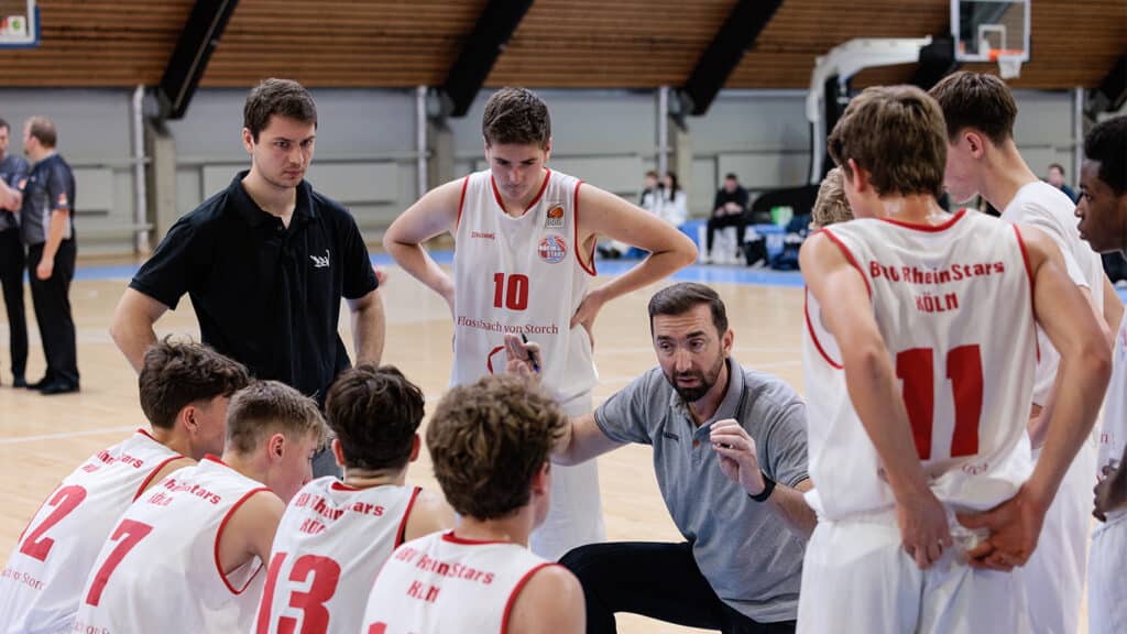 Trainer spricht zu Basketballspielern der RheinStars Köln während einer Spielzeitpause in der Halle.