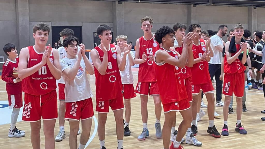 Basketballmannschaft der RheinStars Köln in roten Trikots jubelt in einer Sporthalle.