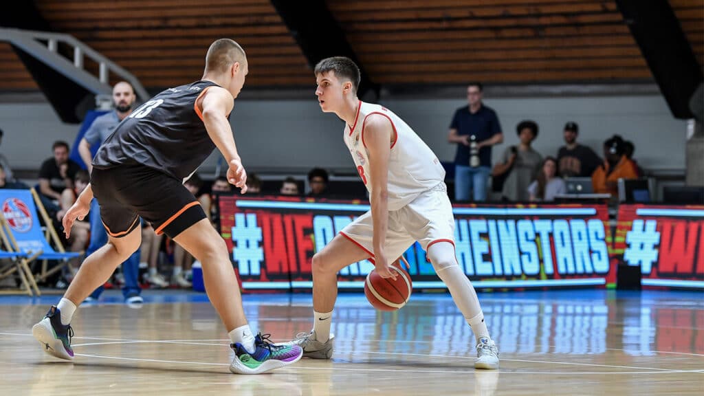 Basketballspiel der RheinStars Köln: Spieler in weißem Trikot dribbelt gegen Gegner in schwarzem Trikot.