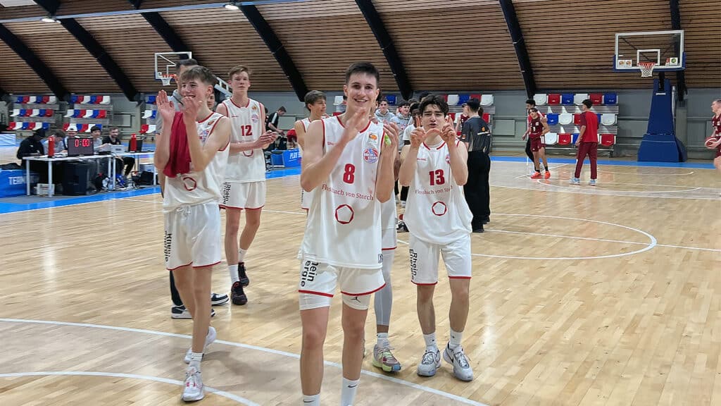 Basketballspieler der RheinStars Köln in weißen Trikots winken nach einem Spiel in einer Sporthalle.