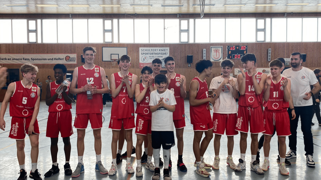Basketballmannschaft RheinStars Köln posiert in roten Trikots in einer Sporthalle.