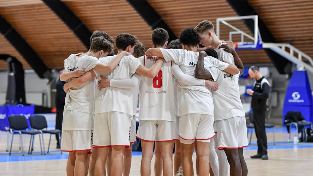 Basketballmannschaft der RheinStars Köln im Teamkreis auf dem Spielfeld einer Sporthalle.