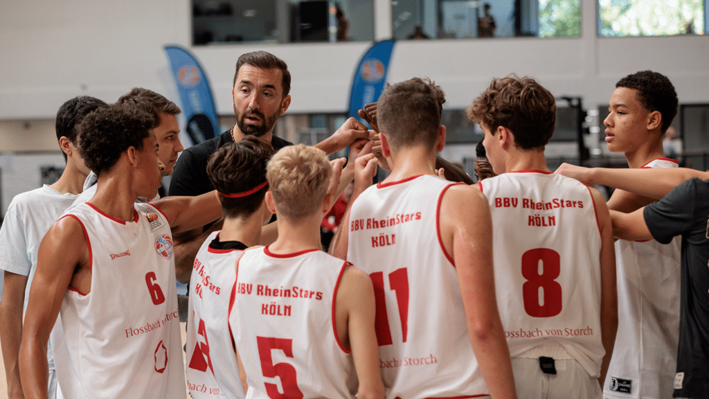 Ein Trainer spricht zu Spielern der BBU RheinStars Köln während einer Trainingseinheit in einer Sporthalle.