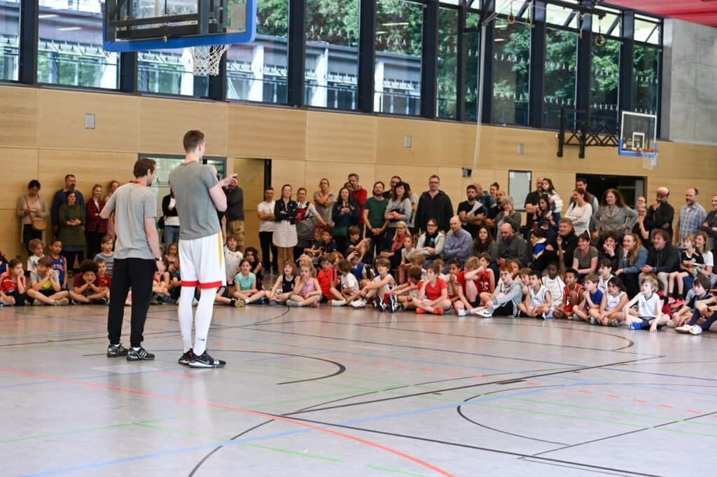 Zwei RheinStars-Spieler präsentieren sich vor Publikum in einer Sporthalle.