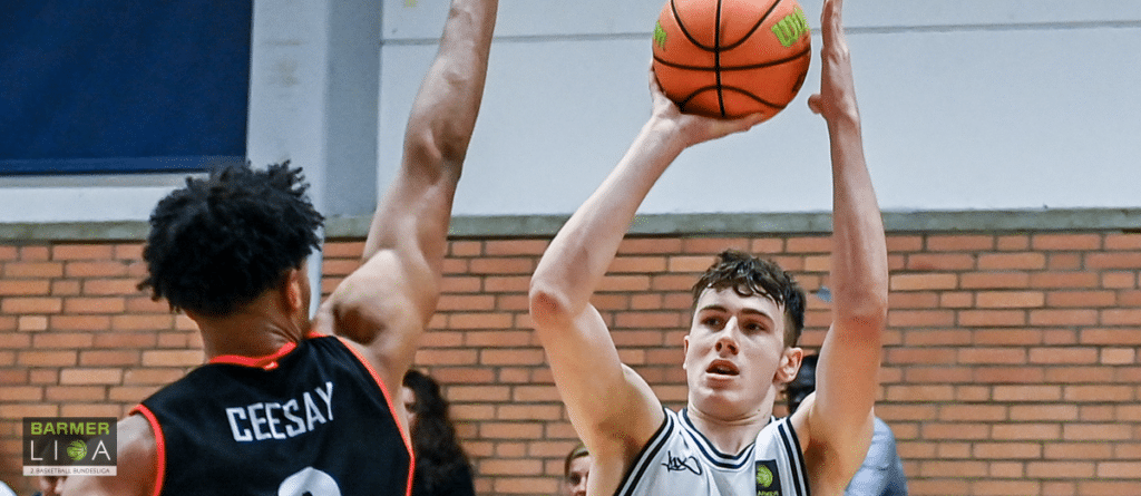 Basketballspieler der RheinStars Köln wirft Ball, während Gegenspieler Ceesay abwehrt.