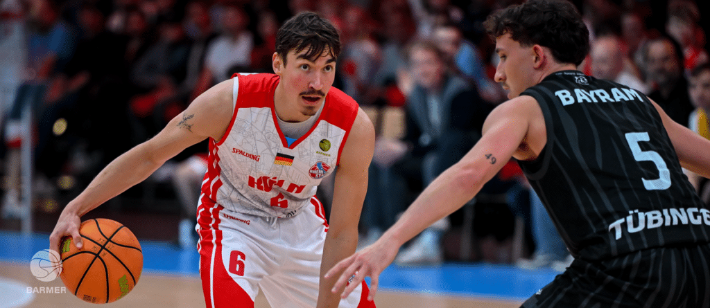 Basketballspieler der RheinStars Köln in rotem Trikot dribbelt gegen Gegner in schwarzem Trikot.