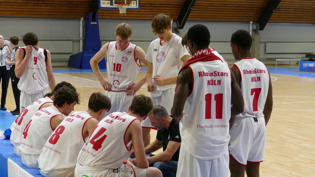 RheinStars Köln Basketballteam in Umkleidekabine bei Trainer-Ansprache.