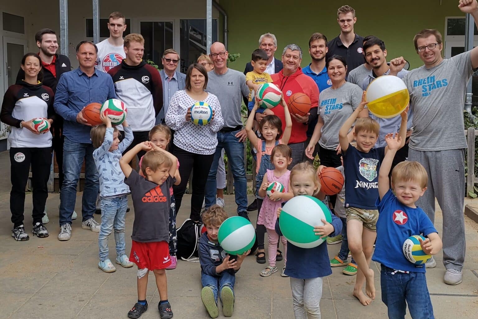 Gruppenfoto der RheinStars Köln mit Kindern und Erwachsenen, die Volleybälle halten.