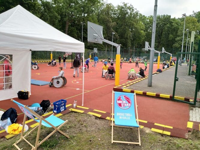Outdoor-Basketballplatz der RheinStars Köln mit Rollstuhlfahrern beim Training unter weißem Zelt.