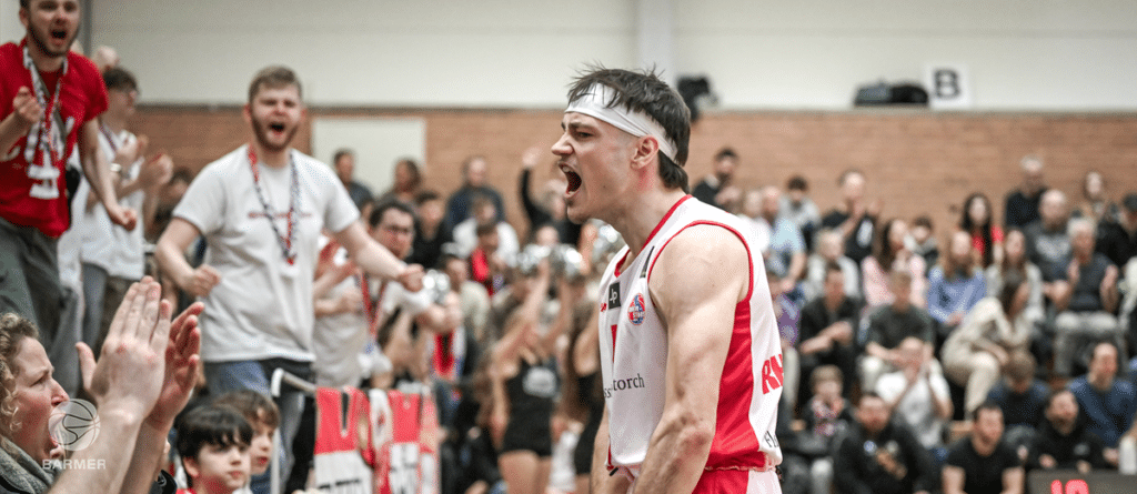 Basketballspieler der RheinStars Köln jubelt emotional vor Zuschauern in der Sporthalle.