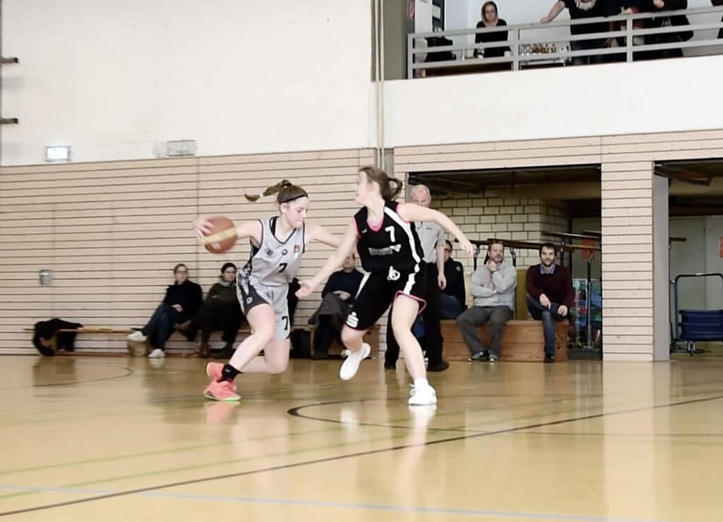 Basketballspiel der RheinStars Köln in der Halle: Spielerin in grauem Trikot dribbelt gegen Verteidigerin in schwarzem Trikot.