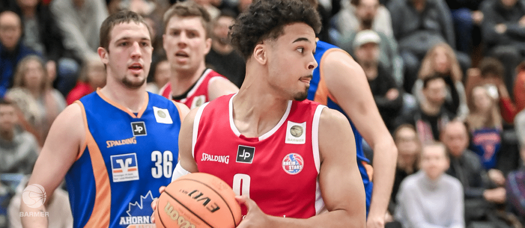 Basketballspieler der RheinStars Köln in rotem Trikot mit Ball während eines Spiels.