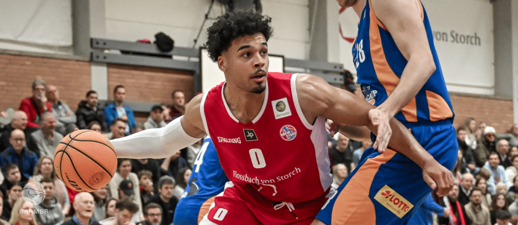 Basketballspieler der RheinStars Köln in rotem Trikot dribbelt gegen blauen Gegner.